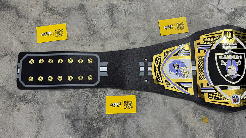 Las Vegas Raiders WWE belt left strap close-up showing gold studs, Raiders shield center plate and printed leather detail