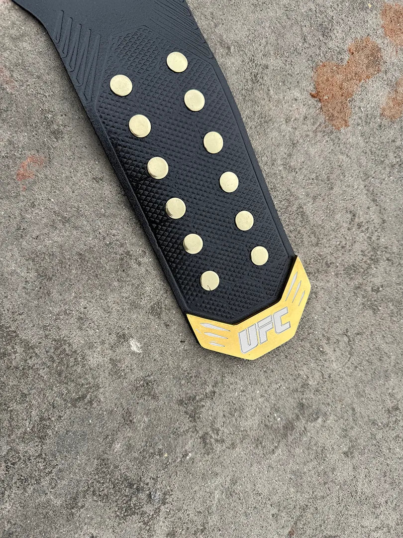 UFC Legacy Championship Belt strap end tip showing gold hardware, studs and black leather texture detail