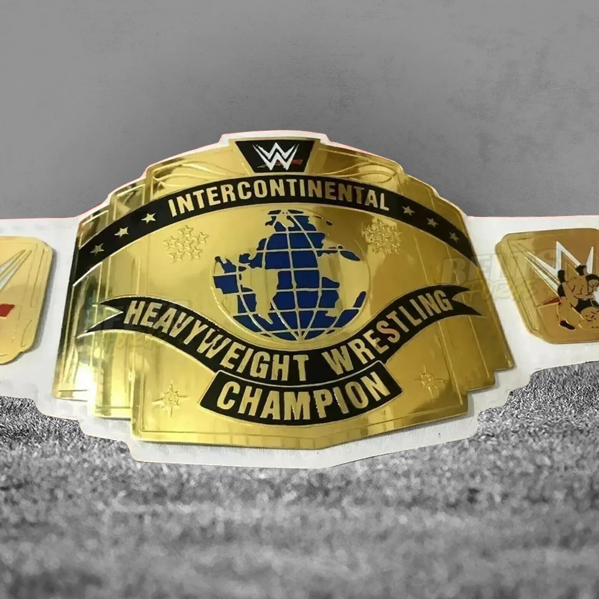 Intercontinental Championship Belt white strap center plate close-up showing CNC-engraved gold-plated brass IC championship design