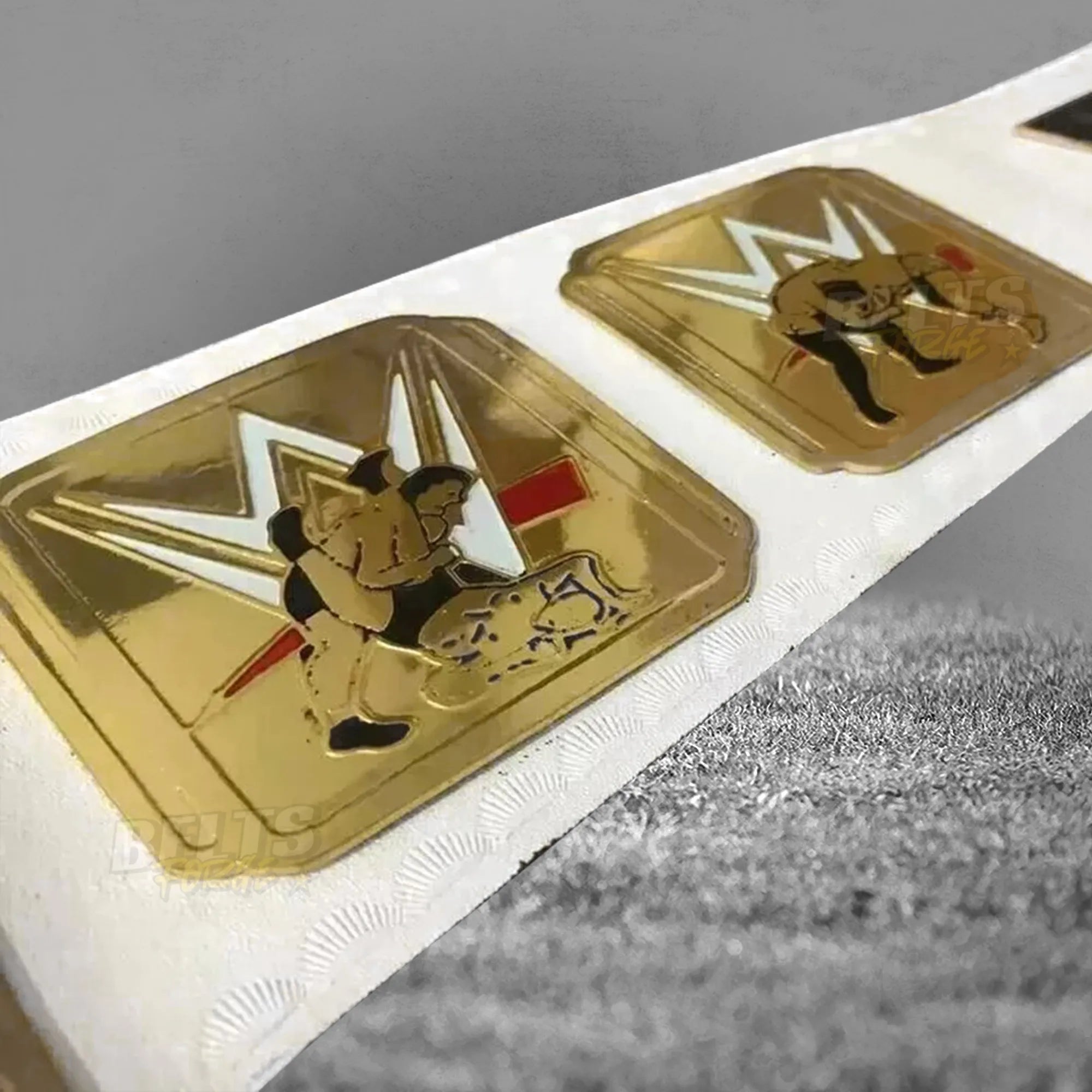 Intercontinental Championship Belt left plates angled close-up showing gold brass IC plate detail on white leather strap